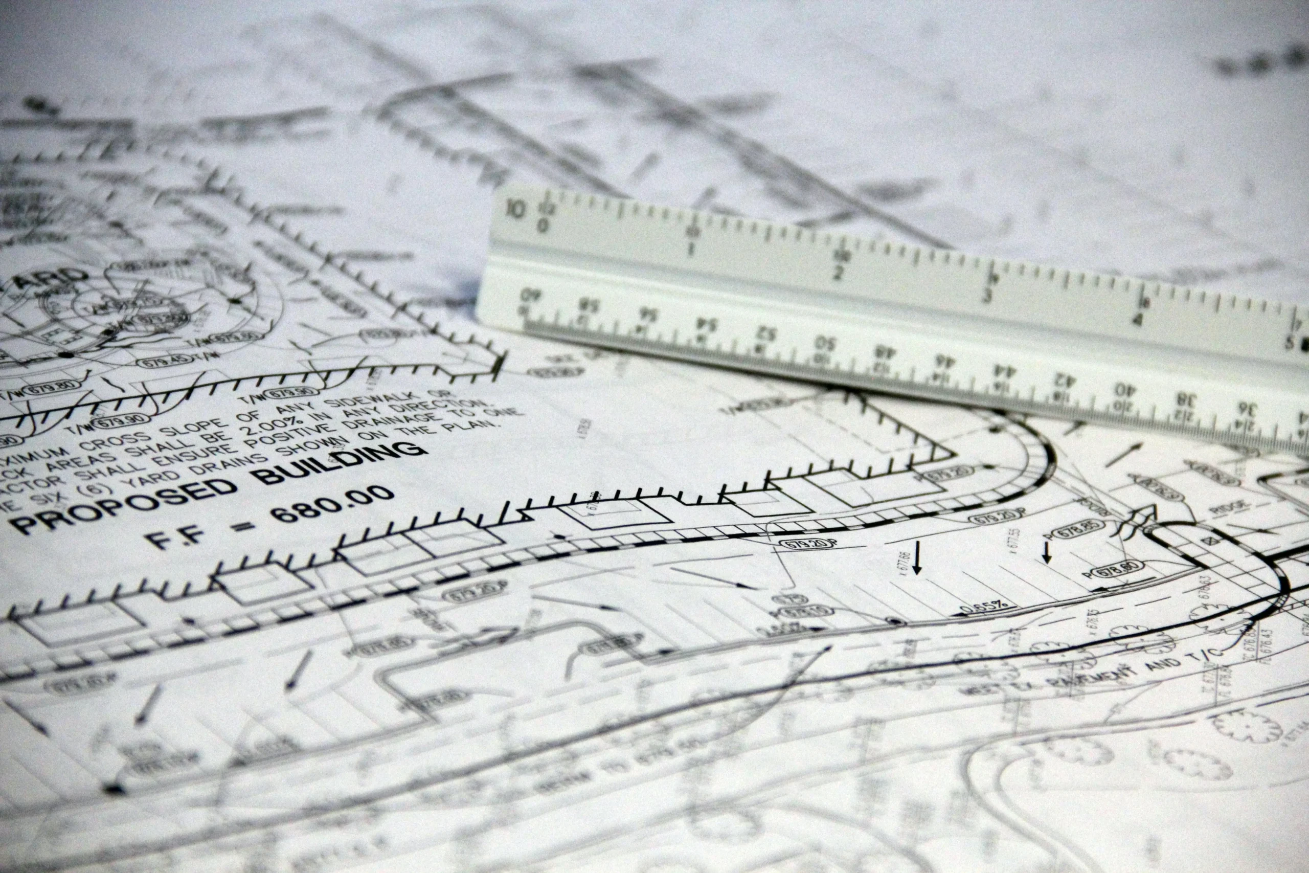 Close-up of a white triangular scale ruler resting on complex proposed building blueprints for land development.