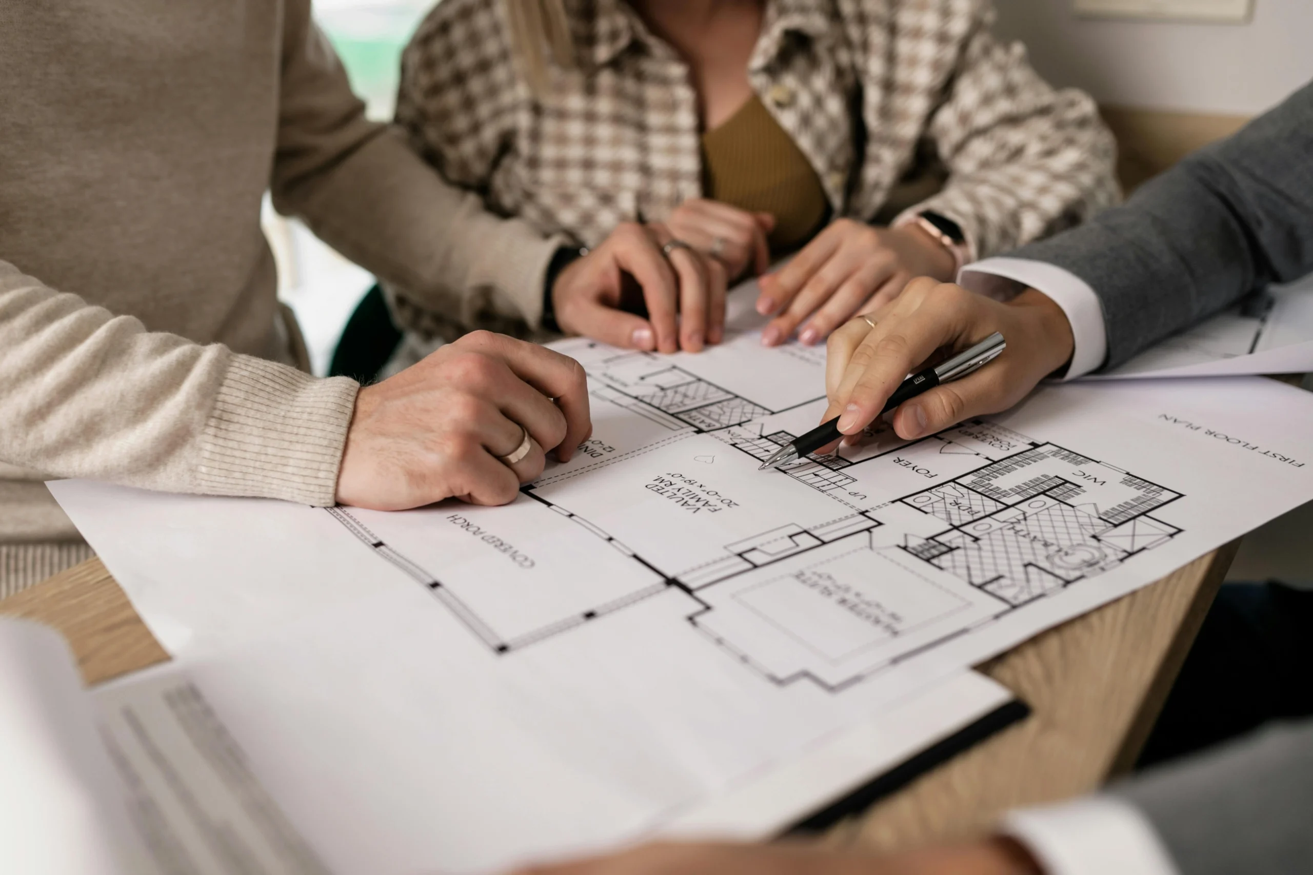 Close-up of a consultant pointing at floor plans during a meeting with two homeowners.